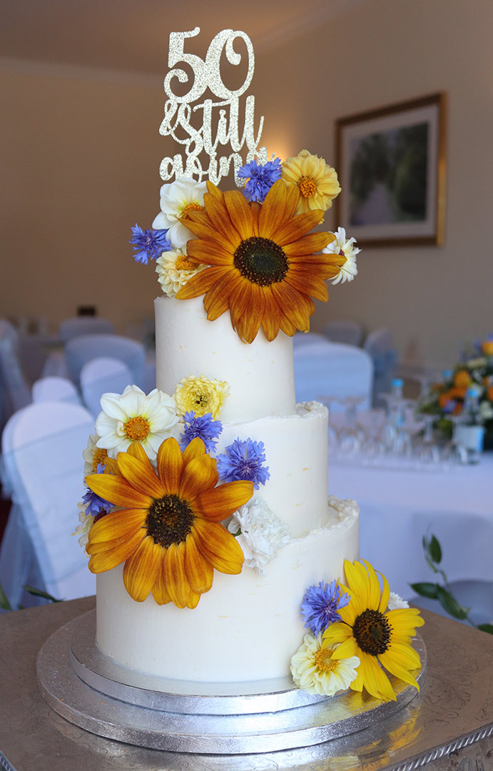 For a gluten free golden wedding anniversary. Three tiers of glutenfree lemon cake, filled with blueberry compote and frosted with lemon vanilla buttercream. All ingredients gluten-free. Splendind sunflowers and other organic edible blooms from Aweside Farm