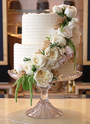 A two-tier white wedding cake for an intimate summer wedding at the Belmond Cadogan Hotel. Gluten-free, wheat-free and milk-free. Two tiers of award-winning dairyfree Tunisian Orange & Almond Cake, filled and frosted with dairy-free lemon buttercream. All ingredients gluten free and milk free. Price includes delivery and assembly at your London venue. Organic edible roses from Maddocks Farm Organics