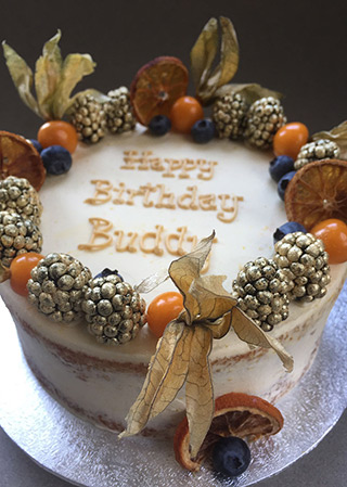 A glutenfree birthday cake: layered dairyfree Orange & Almond cake, filled with orange Swiss meringue buttercream and decorated with physalis, dried orange slices and gold-dusted berries. All ingredients gluten free