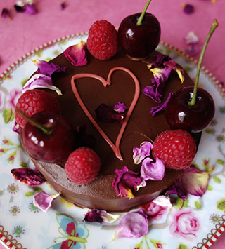 Award-winning gluten free rich chocolate cake made with organic ground almonds and dark chocolate, and Jamaica Rum. Covered with dark chocolate ganache and decorated with piped pink heart in organic white chocolate, cherries, berries & edible rose petals. All ingredients glutenfree. Available diary free