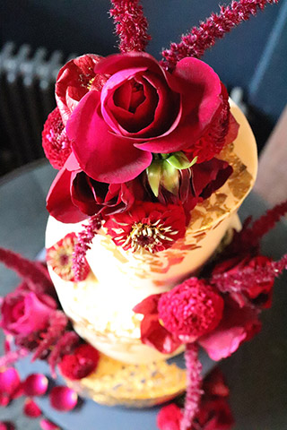 A red, gold & navy gluten free wedding cake at Clapton Country Club. Decorated with real 24 carat gold leaf, and fabulous flounces of amaranth and deep red roses, dahlias, abutilons, all organic edible flowers from Maddocks Farm Organics. Cake flavours: raspberry & vanilla, red velvet, and luxury Jamaica fruit cake. All gluten-free, and the fruit cake is milk-free too. All ingredients glutenfree. Price includes tasting consultation, and delivery and assembly at your London venue