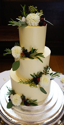 Gluten-free, 3-tier White Chocolate and Chocolate & Orange Wedding Cake, covered with white chocolate Swiss meringue buttercream frosting. Decorated with berries and foliage, and organic edible flowers. For a wedding at Stationers' Hall in the City of London