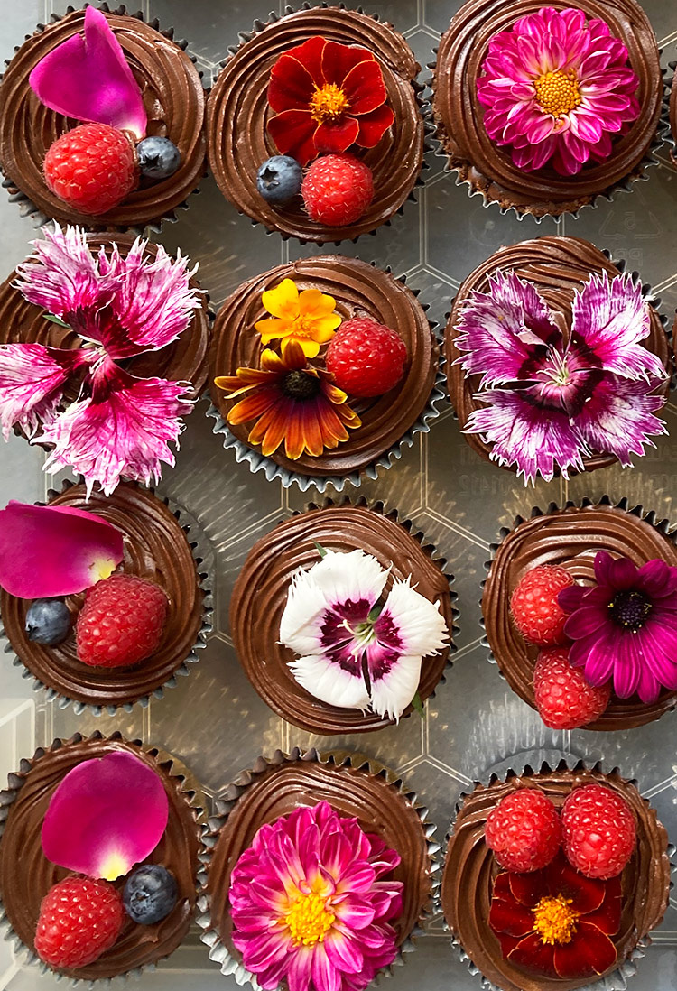 Gluten free chocolate cupcakes topped with choc fudge buttercream and decorated with organic edible flowers and fresh berries. Delivery in London